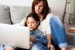 © Guille Faingold/Stocksy - Mother and daughter using laptop on sofa.