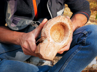 A man in nature carves a kuksa mug from wood. Handmade. Close-up