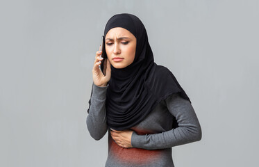 Wall Mural - Muslim woman suffering from abdominal pain, talking on cellphone with doctor