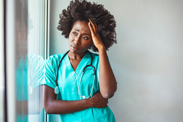 Shot of a young female nurse looking stressed out while standing at a window in a hospital. Female nurse suffering from a serious headache while working inside a hospital