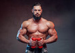 © Fxquadro - Military bodybuilder with beard holding dumbells and posing in dark gradient background.