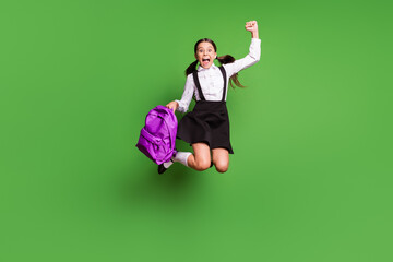 Sticker - Photo portrait of excited girl jumping up holding violet school bag cheering isolated on vivid green colored background