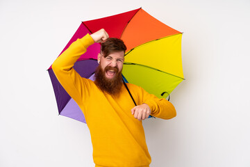 Redhead man with long beard holding an umbrella over isolated white background celebrating a victory