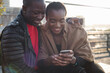 © simon/Stocksy - Happy couple using a phone outdoors