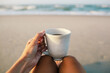 © Kelly Knox/Stocksy - woman holding a cup of coffee in the morning on the beach