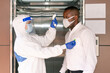 © godji10 - A medical worker in PPE suits using thermometer to check the employee in front of elevator before work on a business day that covid-19 coronavirus is epidemics. Security measures of new normal life.