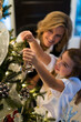 © blurMEDIA/Stocksy - Mother and Little Girl Decorating Christmas Tree for Christmas