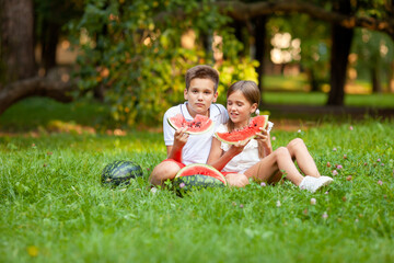 boy and girl sit on the grass and eat watermelon