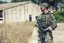 Navy SEALs Fighter In Ballistic Goggles, Equipped Military Ammunition And Body Armour, Holding Service Rifle, Looking In Camera While Standing Outdoors. Special Forces Soldier Half-length Portrait
