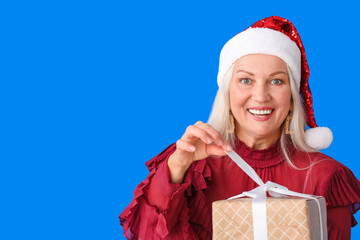 Elderly woman with Christmas gift on color background