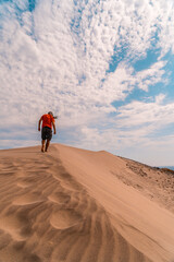 Wall Mural - A man with a red shirt and a turban on his head, walking in the desert of the dune of Playa de Mónsul in the natural park of Cabo de Gata, Nijar, Andalucia. Spain, Mediterranean Sea