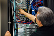 © Curtis Kim/Stocksy - Computer expert working with cables on back of server