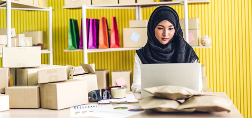 Wall Mural - Portrait of smiling beautiful muslim owner asian woman freelancer sme business online shopping working on laptop computer with parcel box on table at home - Business online shipping and delivery