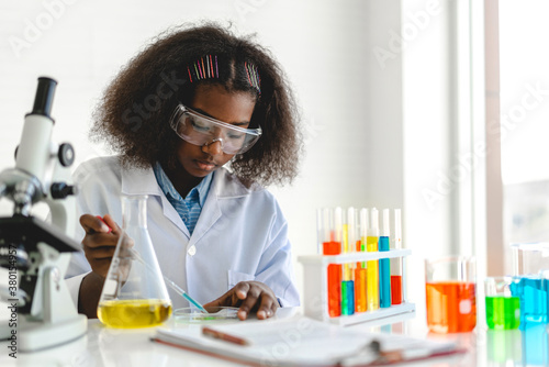Cuadros en Lienzo African american cute little girl student child learning research and doing a chemical experiment while making analyzing and mixing liquid in glass at science class on the table