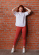 © oleg_ermak - Fashion style studio portrait of beautiful red-haired young girl in leggings pants and white t-shirt. Model standing and posing beside brick wall