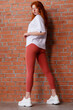 © oleg_ermak - Fashion style studio portrait of beautiful red-haired young girl in leggings pants and white t-shirt. Model standing and posing beside brick wall