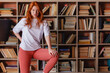 © oleg_ermak - Redhead female college student taking book from shelf in library. Stands on the stairs to get a book from the top. Copy space.