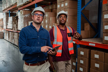 Businessman Wearing Glasses Holding Digital Tablet While Factory Worker Shows Supervisor Around Warehouse.