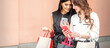 © okskukuruza - Two beautiful caucasian young women watching at smart phone on new seasonal offers with bags during shopping near wall of shopping mall