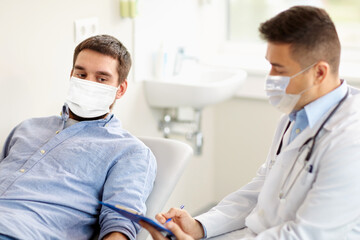 Wall Mural - medicine, healthcare and pandemic concept - doctor wearing face protective medical mask for protection from virus disease with clipboard and young male patient at medical exam at hospital