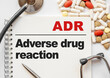 Page in notebook with ADR Adverse drug reaction on white background with stethoscope and group of pill. Medical concept. Term and abbreviation
