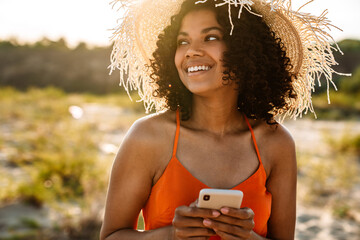 Wall Mural - Smiling young african woman using mobile phone