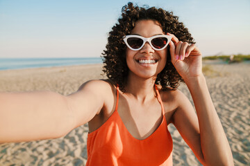 Wall Mural - African woman taking a selfie by camera at the beach