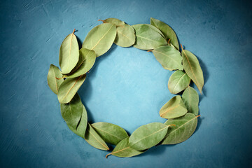 Wall Mural - Culinary frame with a place for text. A wreath of bay leaves, shot from the top on a blue background