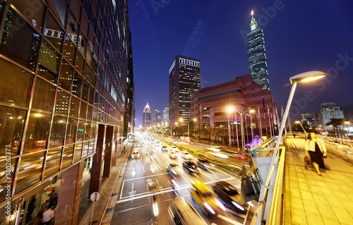Fotomural Evening view of a pedestrian footbridge over a busy street corner at rush hour &