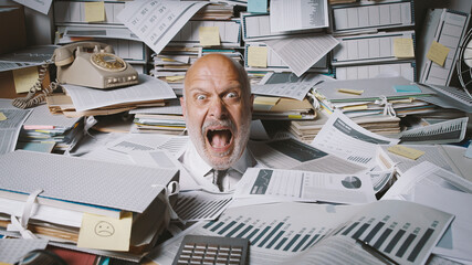 stressed businessman buried under a lot of paperwork