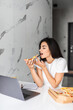 © F8  \ Suport Ukraine - Young woman eating pizza and looking at laptop. Working from home