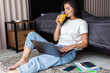 © F8  \ Suport Ukraine - Young beautiful woman drinking juice with her laptop sitting on the floor at bed working at home