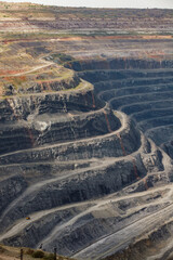 Giant iron ore quarry in Rudny, Kazakhstan. Open-pit mining raw minerals for steel production. Yellow quarry truck down. Quarry steps under beauty sun.