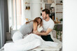 © JustLife - Young couple fighting pillows on the bed. Happy couple having fun at home.