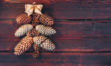 Happy New Year And Merry Christmas. A Christmas Tree Made Of Cones With A Gold Bow On Top Is Laid Out On A Brown Wooden Background. Beautiful Wooden Christmas Background. Christmas Tree Made Of Cones.