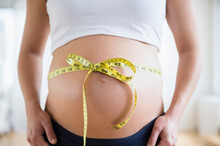 Mid Section Of Pregnant Woman With Tape Measure Tied Up On Her Belly