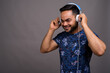 © Ranta Images - Young bearded Indian man listening to music against gray backgro
