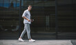© BullRun - Focused man walking on pavement with smartphone in afternoon