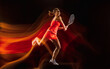 © master1305 - In flight. Professional female tennis player training isolated on black studio background in mixed light. Woman in sportsuit practicing. Healthy lifestyle, sport, workout, motion and action concept.