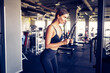 © zamuruev - Fit well-trained woman workout triceps lifting weights in gym. Athletic sexy woman doing exercise using machine in gym - side view.
