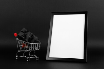 A frame and shopping cart with gifts on black background, a blank for the design, concept. Copy space.