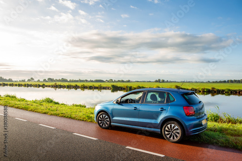 Fotomural A blue parked car on the side of the road near the ringvaart canal in the North-Holland village of Abbenes on a cloudy day in the Netherlands