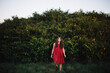 © HOWL/Stocksy - Young woman emerges from the bushes wearing a red dress