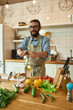 © Svitlana - Young man, Italian cook looking cheerful while opening a bottle of white wine with a corkscrew in the kitchen
