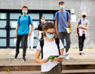 Teenage girl in a protective mask with a backpack and notebooks walking in the street