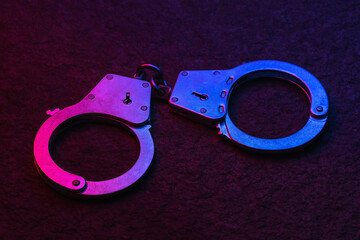 Handcuffs on a stone surface illuminated by flashing lights of a police car, close-up