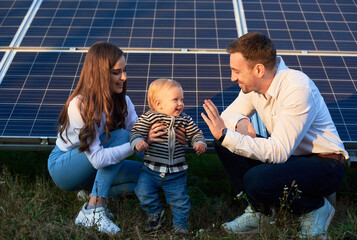 Wall Mural - Dad, mom and baby on the background of solar panels on a warm day. The concept of family warmth and comfort in the modern world with continuously advancing technology