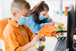 © LIGHTFIELD STUDIOS - Selective focus of schoolboy in medical mask modeling robot from building blocks and computer in school