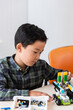 © LIGHTFIELD STUDIOS - Selective focus of asian schoolboy looking at robot near building blocks on table in stem school
