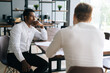 © dikushin - Thoughtful serious professional African American man interviewing caucasian European young candidate for job at successful company. Two business people talking strategy sitting at office desk.